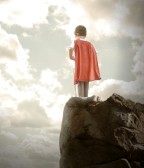 18066088-a-young-super-hero-boy-is-wearing-a-red-cape-and-standing-on-a-rocky-cliff-looking-at-a-cloudy-sky-w